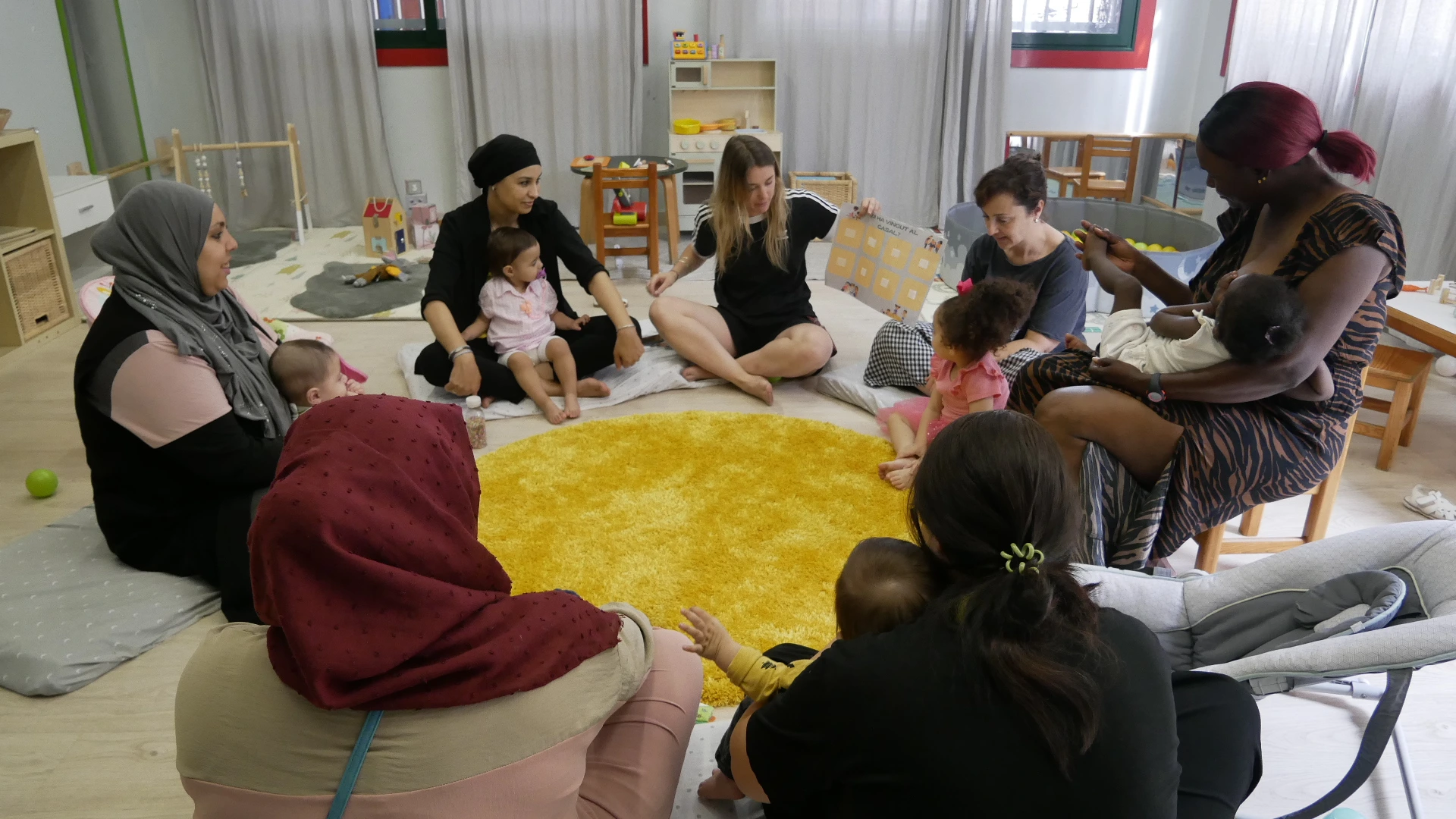Mares amb els seus fills i filles amb una educadora en un projecte de Espais 0-6 anys.