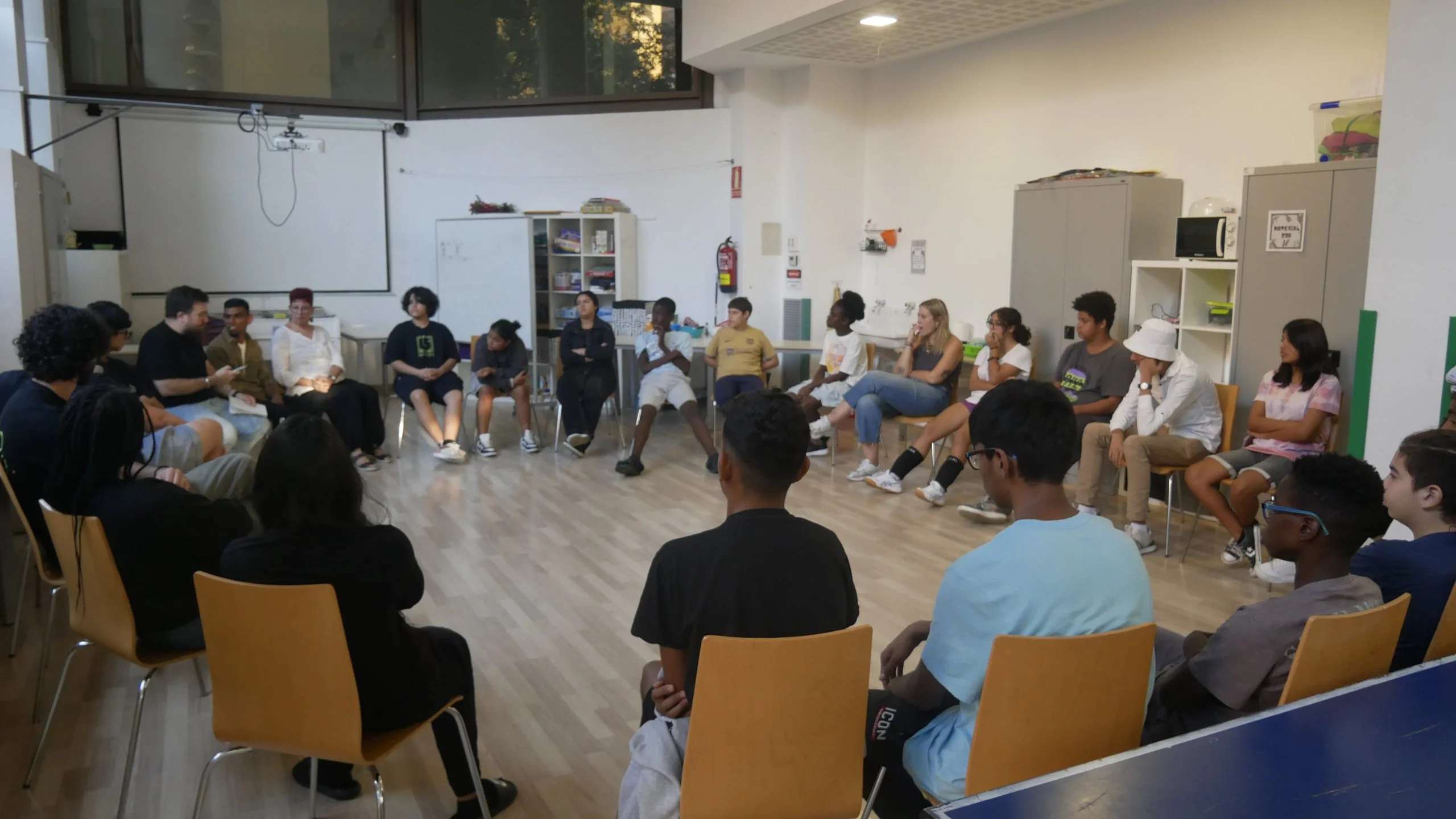 Adolescents asseguts en cadires a formar un circulo i escoltant tots a l'una persona parlant. Centre Obert Adolescent Santa Coloma