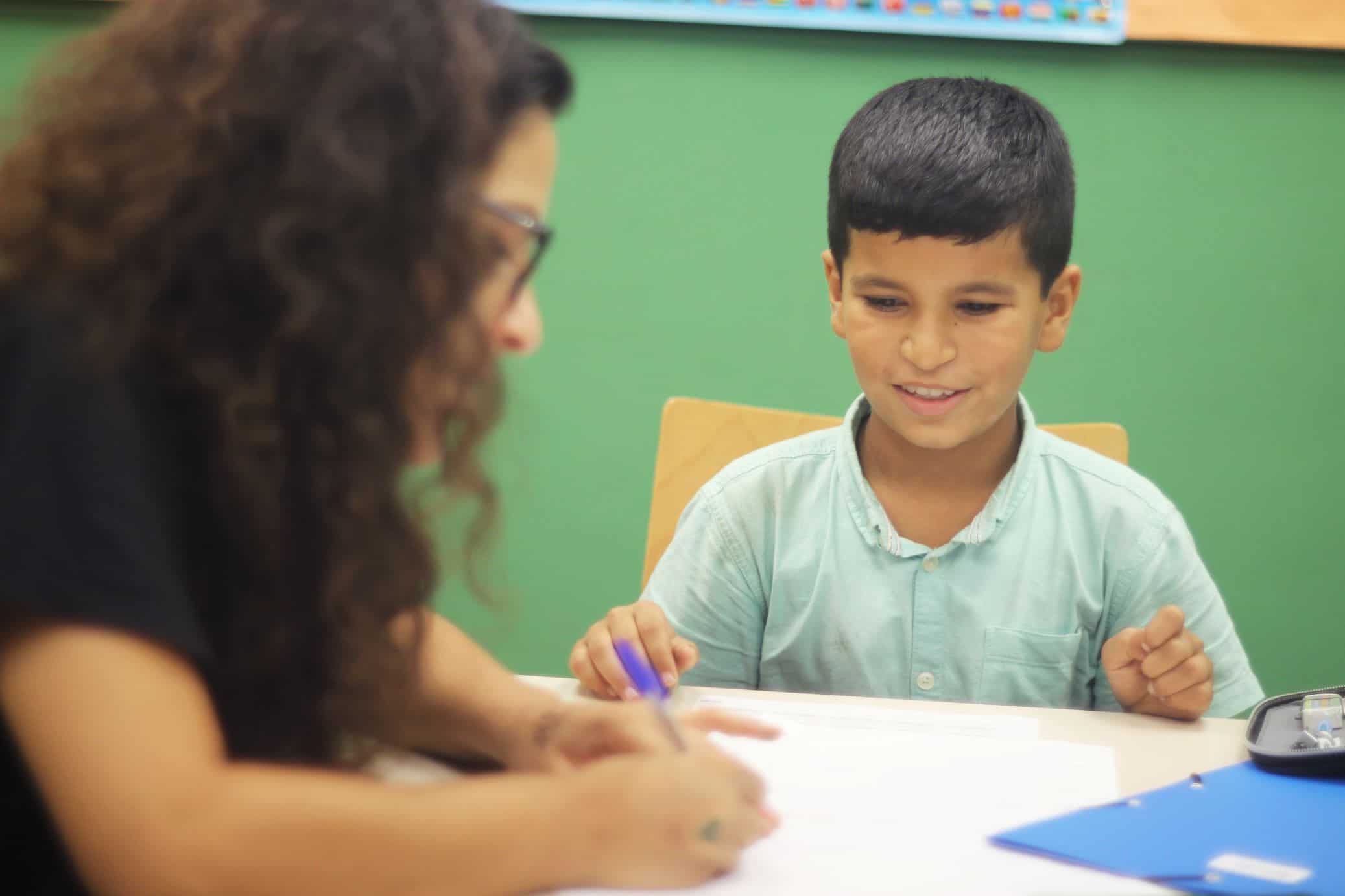 Un niño haciendo tareas de refuerzo escolar con una educadora del Casal dels Infants
