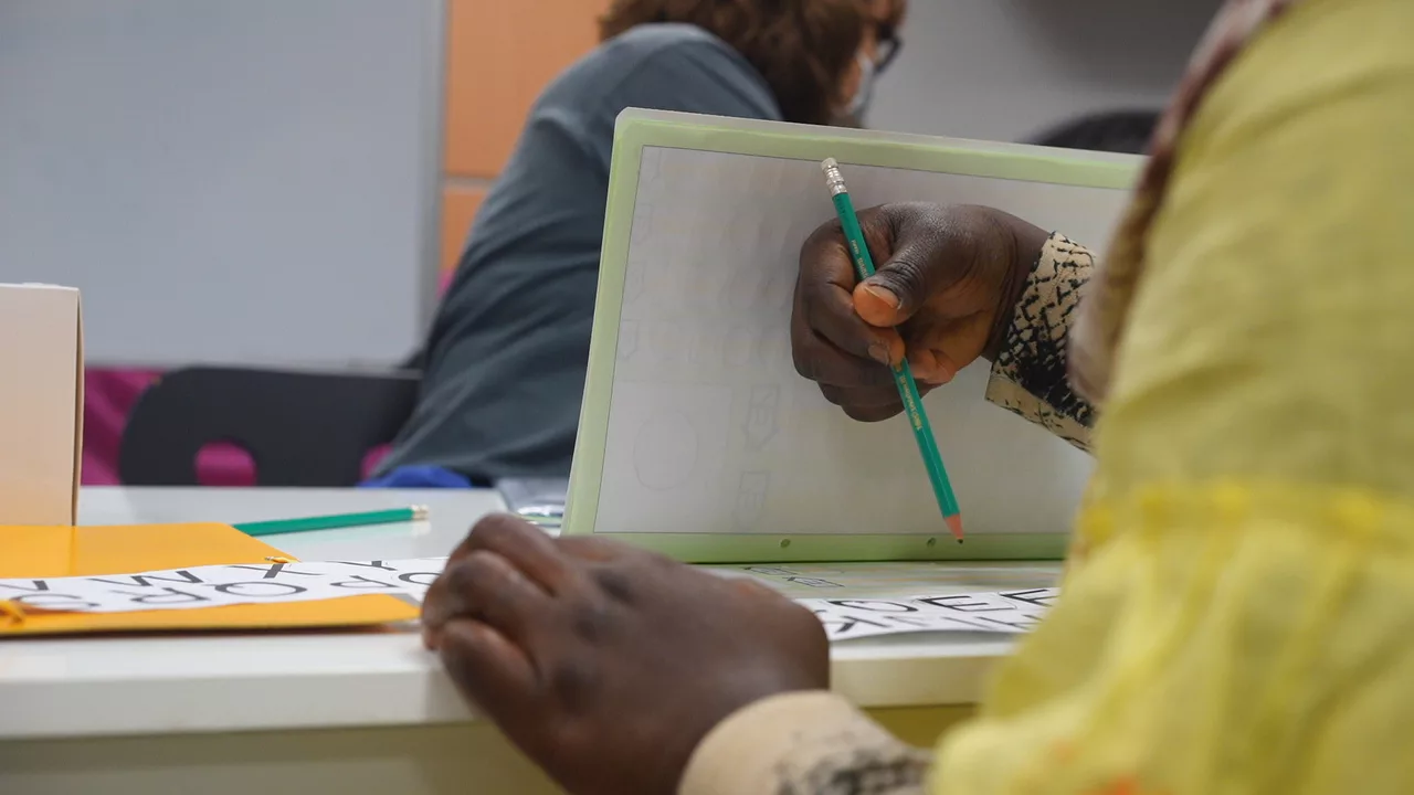 Detall d'unes mans agafant un llapis i una llibreta sobre la taula.