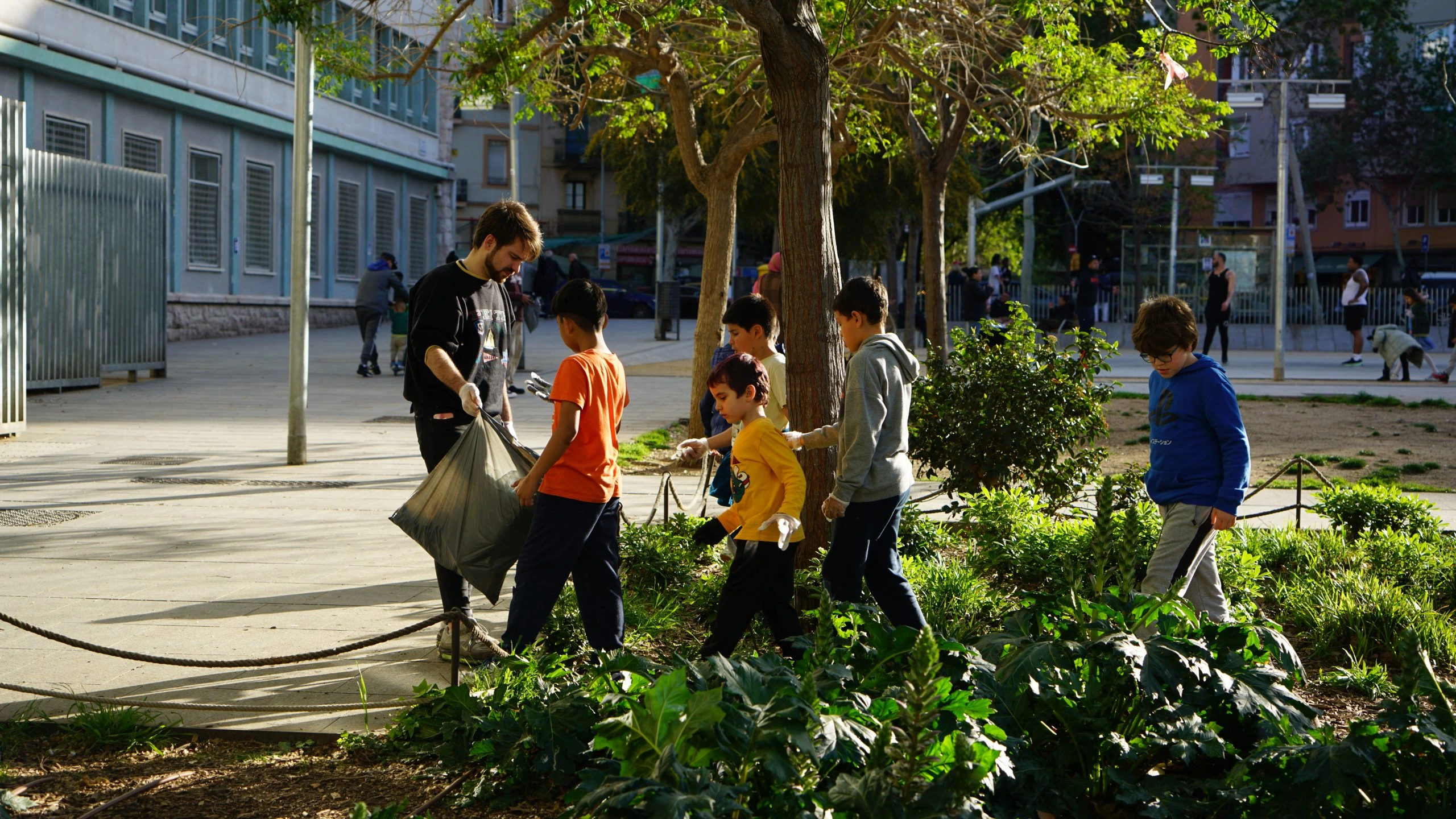 Un educador amb la bossa d'escombraries a la mà i els nens recullen per a posar-lo dins.
