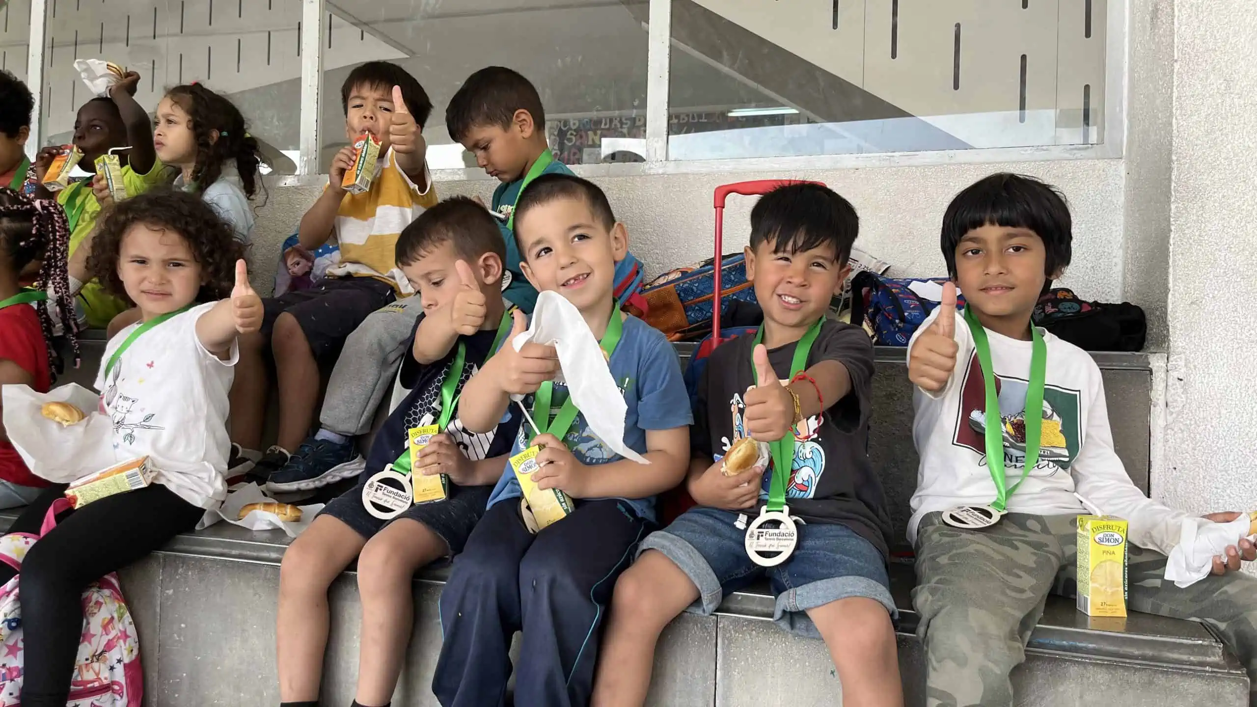 Nens berenen amb una medalla penjada al coll després de la classe de tennis.