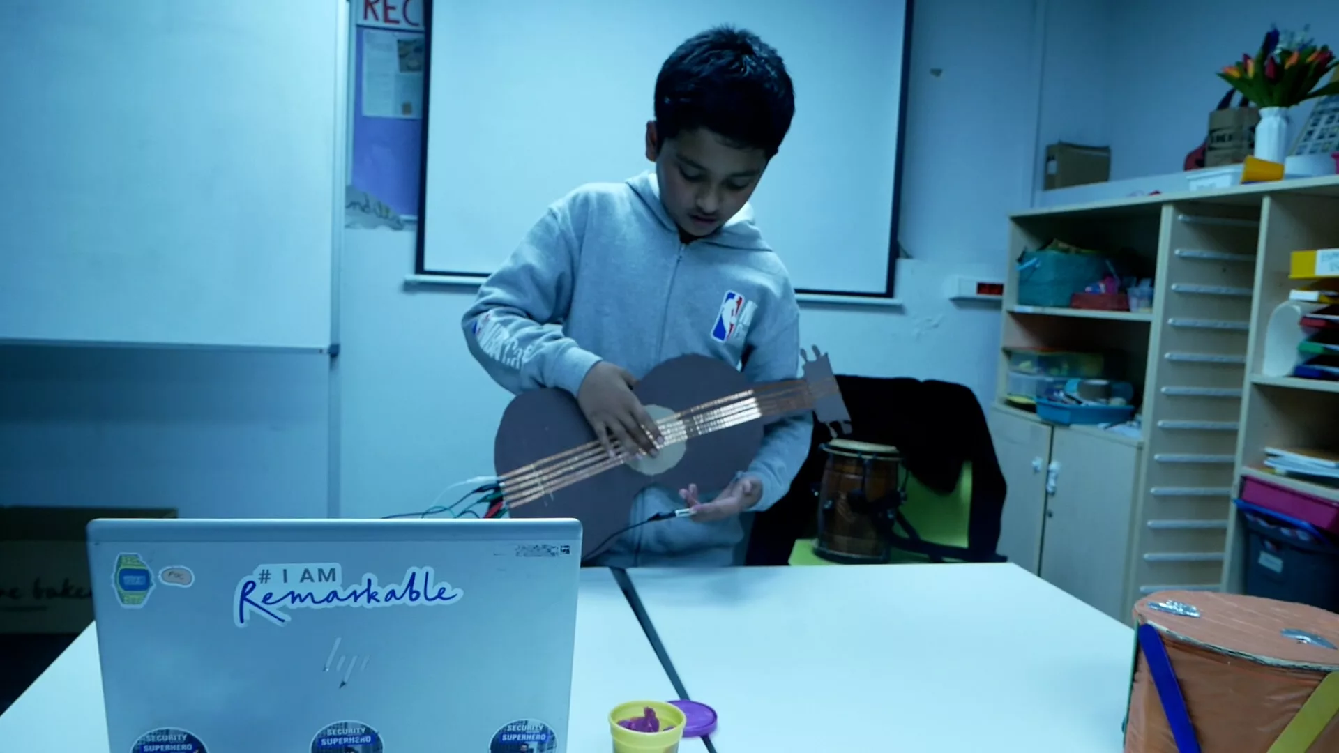 Un noi toca una guitarra feta de cartró gràcies a la connectivitat del paper d'alumini de les cordes.