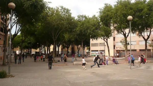 badalona_casal_dels_infants Plaça amb nens i nenes jugant a voley ball i futbol i persones passejant.
