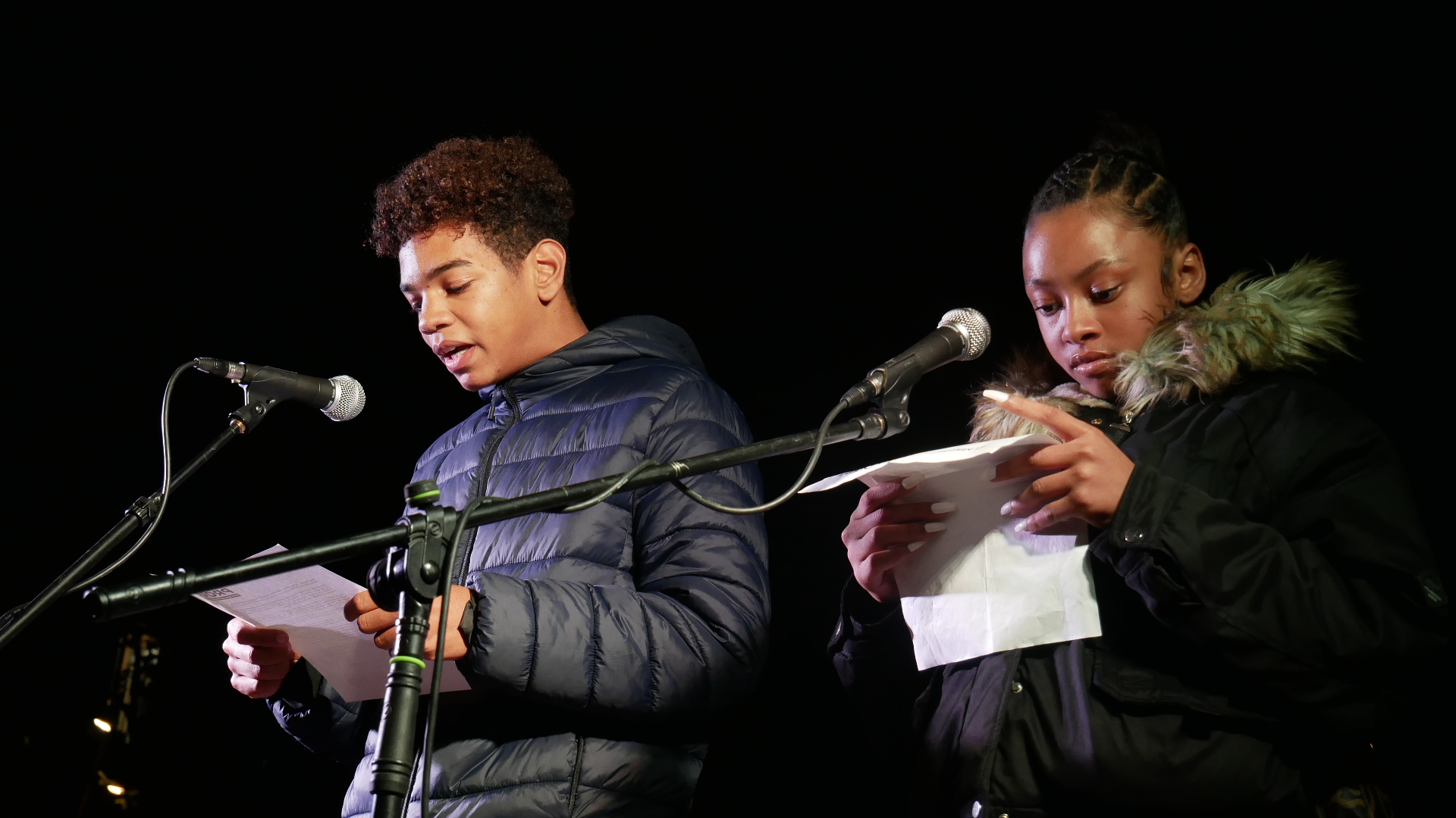 Un noi i una noia llegeixen un manifest amb dos micròfons davant.