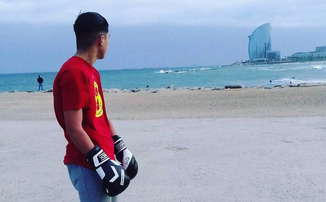 Un jove davant de la platja de Barcelona amb uns guants de boxa posats.