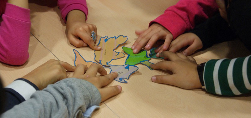 Foto de les mans de sis nens agafant amb les mans el dibuix amb la forma del seu país de procedència. 